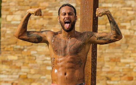 Neymar sem camisa, embaixo do chuveiro, mostrando músculos e com a língua de fora