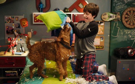 Josh Hutcherson se diverte com um cão em cima da cama em cena do filme O Cachorro Bombeiro