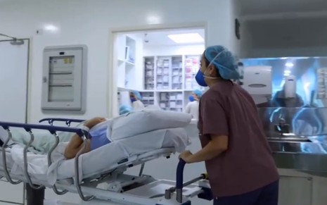 Imagem de uma enfermeira empurrando uma maca pelo corredor de um hospital