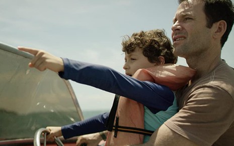 Mauricio Alemañy com um colete salva-vidas, no colo de Eion Bailey, apontando para algum lugar; os dois estão em alto-mar