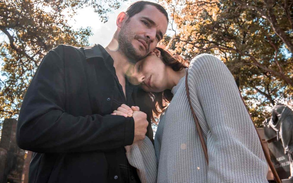 Os atores Daniel de Oliveira e Leticia Colin abraçados, ele segurando a mão dela, ela com cabela apoiada no ombro dele, em cena em lugar arborizado da série Onde Está Meu Coração