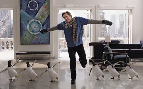 Jim Carrey ao centro com os braços levantados e uma perna erguida; à sua esquerda três pinguins o imitam e à sua direita também