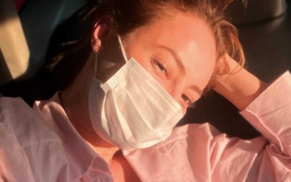 A atriz Paolla Oliveira está deitada em um sofá com uma máscara cirúrgica branca no rosto em foto de seu Instagram