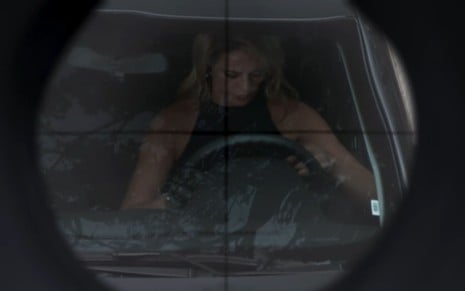 A atriz Paolla Oliveira está com a cabeça baixa dentro do carro; ela aparece no centro de um alvo