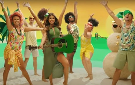 Paula Fernandes com vestido e violão verdes, cantando em cenário de praia com bailarinos ao redor