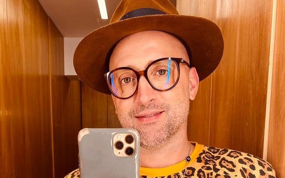 Paulo Gustavo, de óculos e chapéu, tira selfie no espelho, com seu celular aparecendo na foto