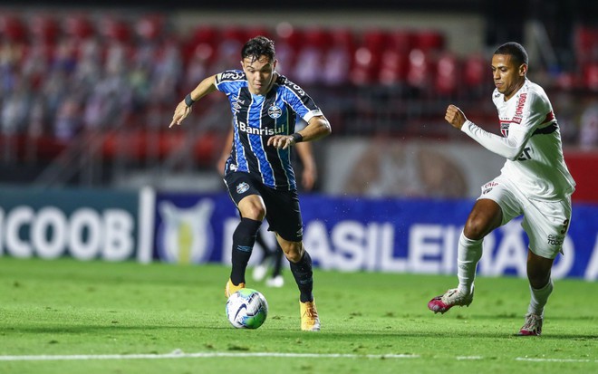 Pepê do Grêmio e Bruno Alves do São Paulo em disputa de bola no campo, Pepê vestido com o uniforme do Grêmio nas cores azul, preto e branco e Bruno Alves vestido com o uniforme do São Paulo na cor branca