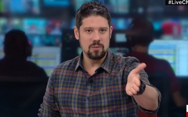 Phelipe Siani com camisa xadrez, mão esquerda levantada