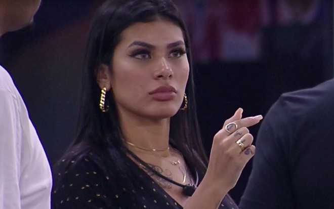 Pocah olha para outro participante; ela está com vestido preto e cabelo (preto) solto