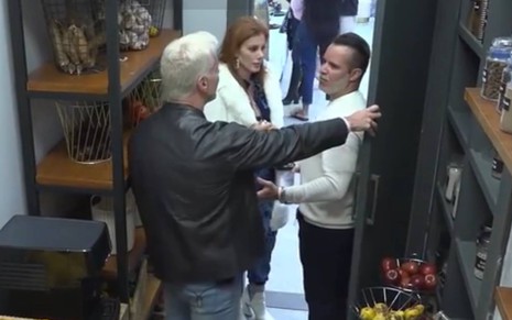 Bruno está de costas, usa jaqueta preta e está segurando a porta na qual Filipe está encostado, o músico usa blusa branca; Deborah está no meio dos dois e usa casaco branco