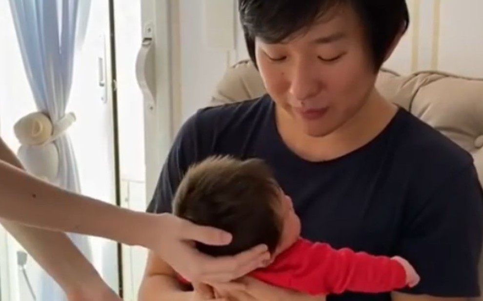 Imagem de Pyong Lee em casa, segurando o filho Jake pela primeira vez