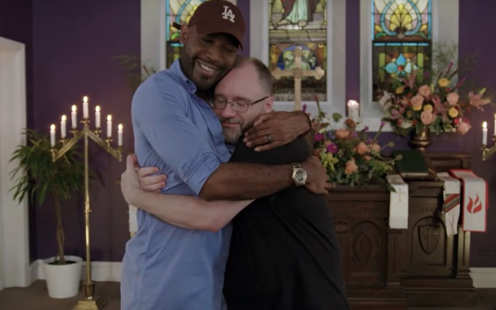 Um dos apresentadores do Queer Eye, Karamo Brown, abraça padre em igreja, em episódio do reality