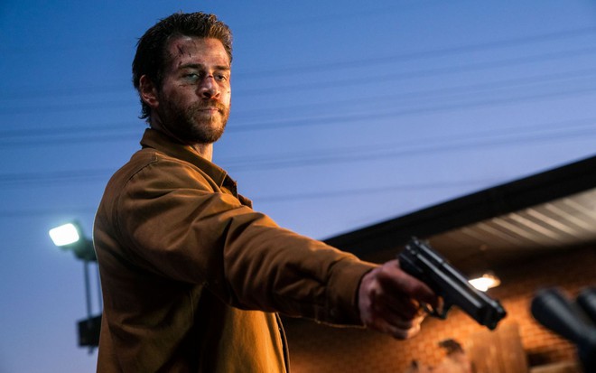 Ensaguentado, Liam Hemsworth aponta uma arma para baixo em cena de Most Dangerous Game