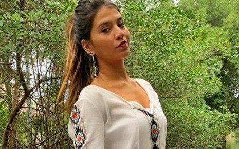 Raquel de Queiroz de cabelo preso, posa para foto em paisagem com árvores ao fundo