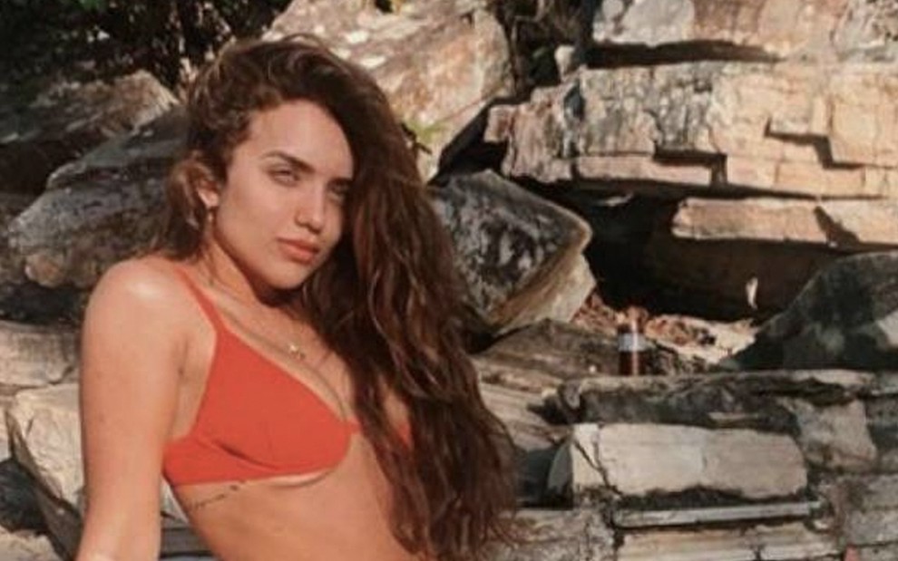 A influenciadora Rafa Kalimann sentada em frente a uma cachoeira com um biquini laranja em foto do Instagram
