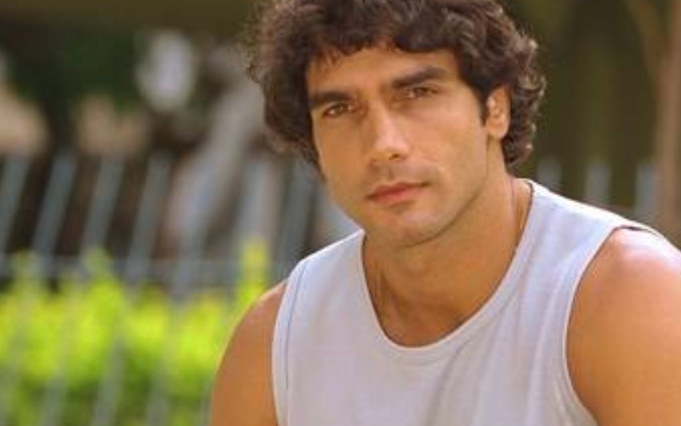 O ator Rafael Calomeni com expressão séria e regata branca, caracterizado como Expedito em Mulheres Apaixonadas (2003)