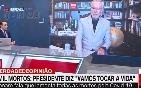 Rafael Colombo sentado de frente para o telão que exibia Alexandre Garcia ao vivo na CNN Brasil