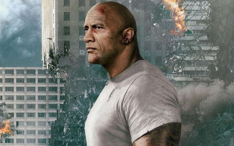 Com uma cidade destruída ao fundo, o personagem de The Rock faz cara de bravo em Rampage - Destruição Total