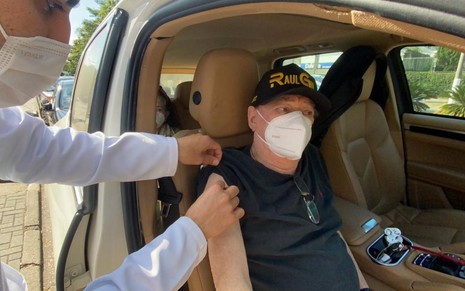 Raul Gil, sentado em seu carro, de máscara, recebe a segunda dose da vacina contra a Covid-19