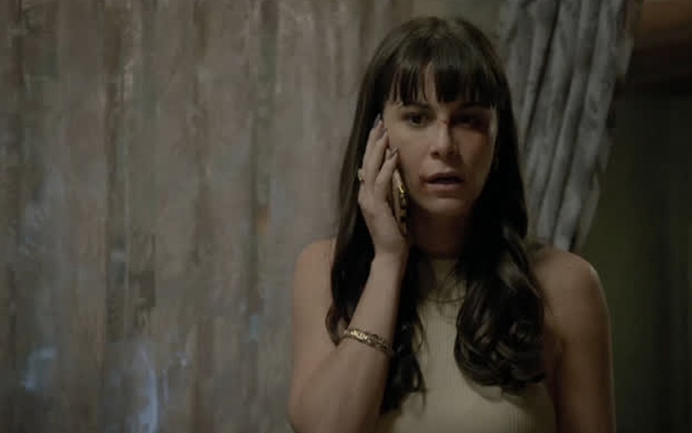 Com o rosto machucado, a atriz Dani Moreno fala ao celular caracterizada como Furacão em cena de Amor Sem Igual