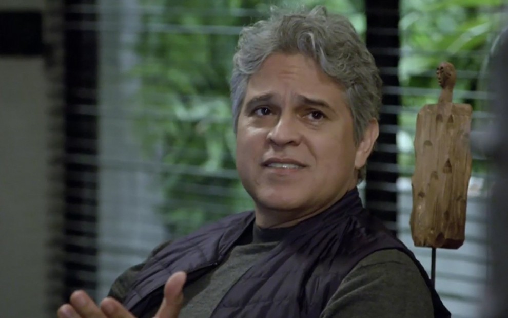 O ator Juan Alba sentado em uma poltrona e diante de uma janela; ele está caracterizado como Ramiro em cena de Amor Sem Igual