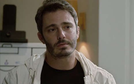 Thiago Rodrigues em cena de Amor Sem Igual: com camiseta preta e blusa branca, personagem olha para alguém fora do quadro