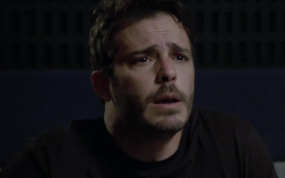 Thiago Martins em cena de Amor Sem Igual: com camiseta preta, personagem olha para alguém com cara de confusão
