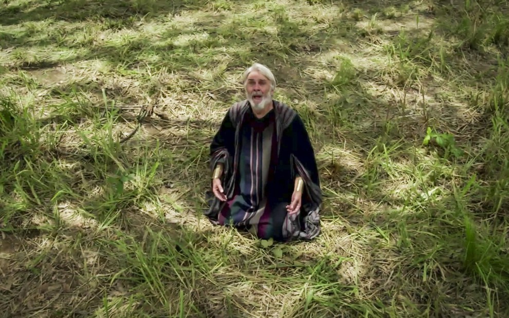Zécarlos Machado grava ajoelhado na grama olhando para o céu com expressão de felicidade