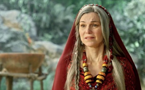 A atriz Adriana Garambone como Sarai, com uma roupa vermelha ricamente adornada por joias, com expressão de confusão em cena de Gênesis
