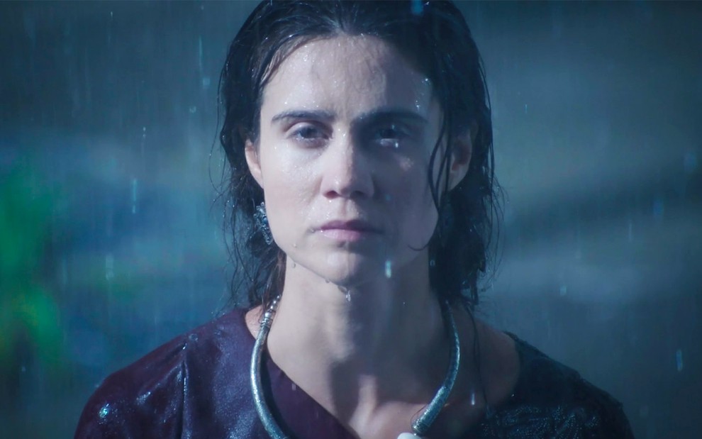 Branca Messina em cena de Gênesis: caracterizada com Amat, atriz está no meio da chuva e olha com frieza para frente