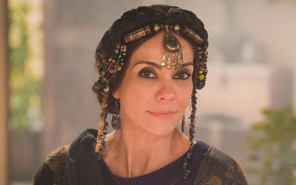 Flávia Monteiro caracterizada como Aya em Gênesis: com adorno dourado na cabeça, atriz usa maquiagem preta ao redor dos olhos e sorri para câmera