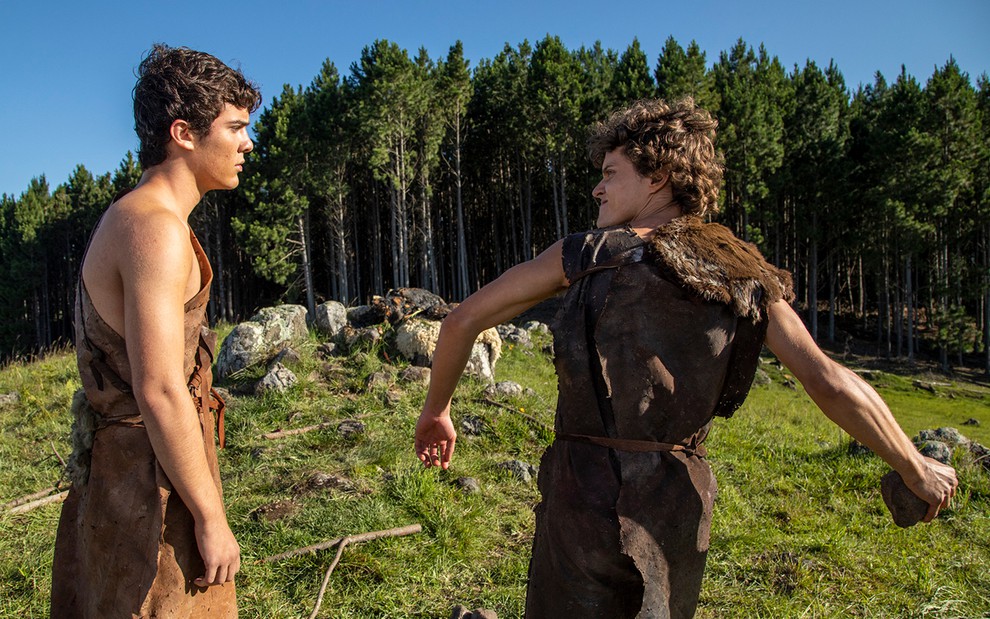 O ator Caio Manhente como Abel à esquerda se prepara para ser atingido por Eduardo Speroni como Caim, que lança uma pedra em cena de Gênesis