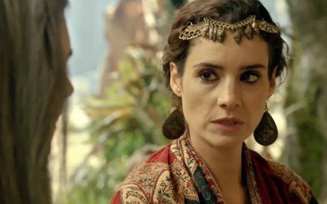 A atriz Elisa Pinheiro como Ayla em uma cena externa de Gênesis, ela está com roupas caras e ricamente adornadas, além de uma expressão de revolta