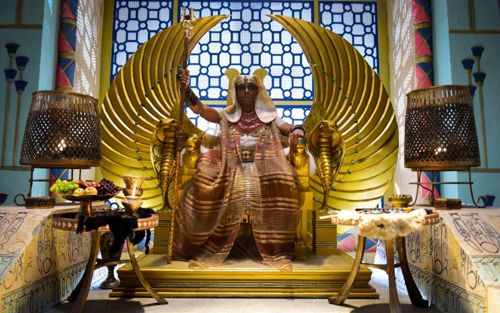 André Ramiro grava vestido como um faraó sentado em um trono de ouro com asas esculpidas em Gênesis