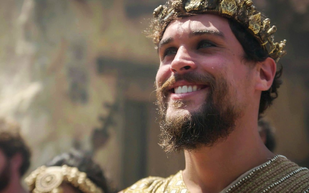 Close up do ator Felipe Roque como Ibbi Sin em cena de Gênesis, ele está com uma coroa de louros banhada de ouro e usa um cavanhaque