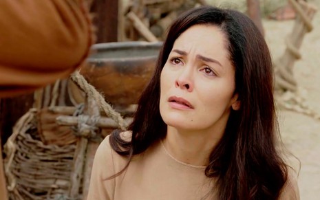 A atriz Hylka Maria como Agar, ela se ajoelha e tem lágrimas nos olhos como se implorasse pela própria vida em cena de Gênesis