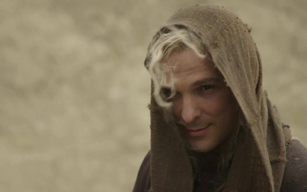 O ator Igor Rickli está caracterizado como Heylel, um dos disfarces de Lúcifer, com cabelos longos e muito platinados e um lenço de algodão encardido na cabeça em cena de Gênesis
