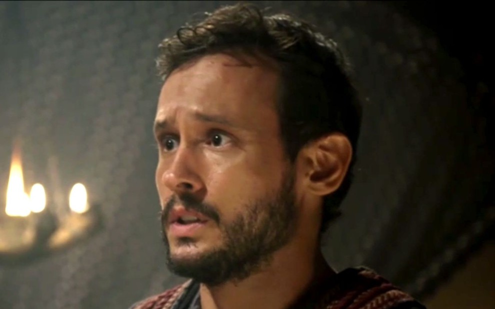 Guilherme Dellorto em cena de Gênesis: ator está caracterizado com Isaque, e olha para alguém fora do quadro com surpresa
