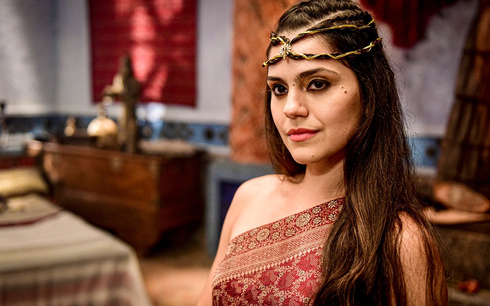 A atriz Jessika Alves com uma joia de ouro e uma pedra preciosa no centro na cabeça, além de uma túnica marrom de um ombro só, como Shakia em cena de Gênesis