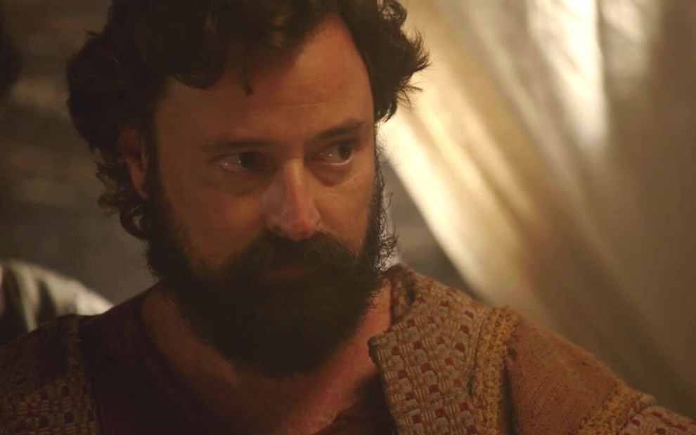 Emilio Orciollo Neto em cena de Gênesis: caracterizado como Ló, ator olha com seriedade para alguém fora do quadro