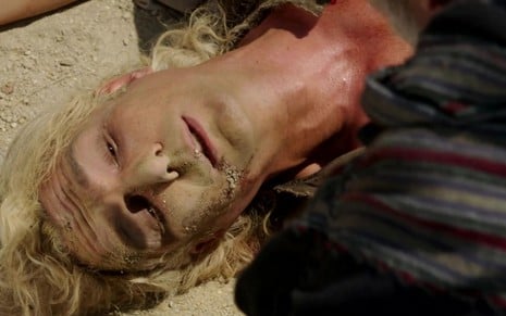 Igor Rickli em cena de Gênesis: caracterizado como Lúcifer, personagem está deitado e de olhos fechados coberto por terra