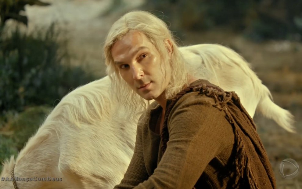 Igor Rickli grava de cabelo longo, branco e preso em rabo de cavalo olhando para o lado desconfiado como Lúcifer