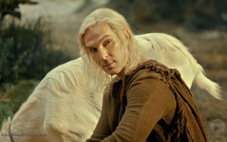 Igor Rickli grava de cabelo longo, branco e preso em rabo de cavalo olhando para o lado desconfiado como Lúcifer