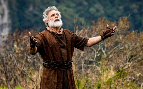 O ator Oscar Magrini de braços abertos caracterizado como Noé em cena de Gênesis