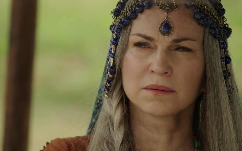 Adriana Garambone em cena com acessório azul na cabeça e olhar desconfiado e desconfortável como Sara de Gênesis