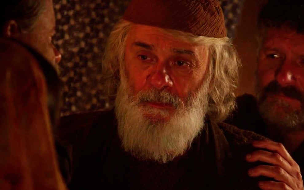 O ator Zécarlos Machado com cabelos e barba bem brancos e longos, ele usa um chapéu redondo como Abraão em cena de Gênesis