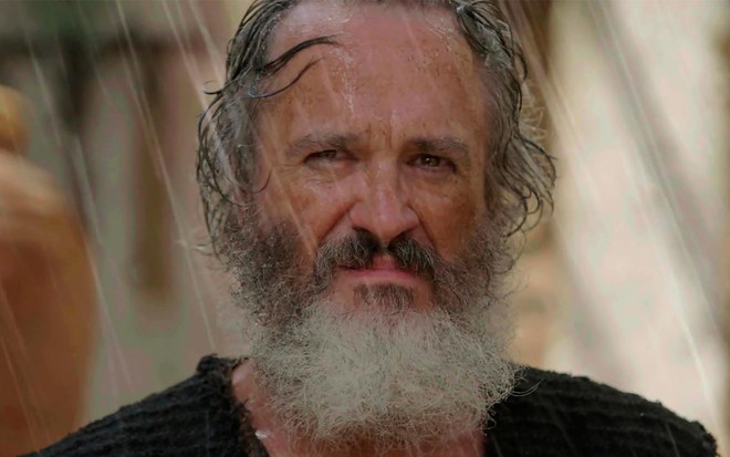 Leonardo Medeiros em cena de Gênesis: caracterizada como Zeno, ator está na chuva e olha com seriedade para alguém fora do quadro