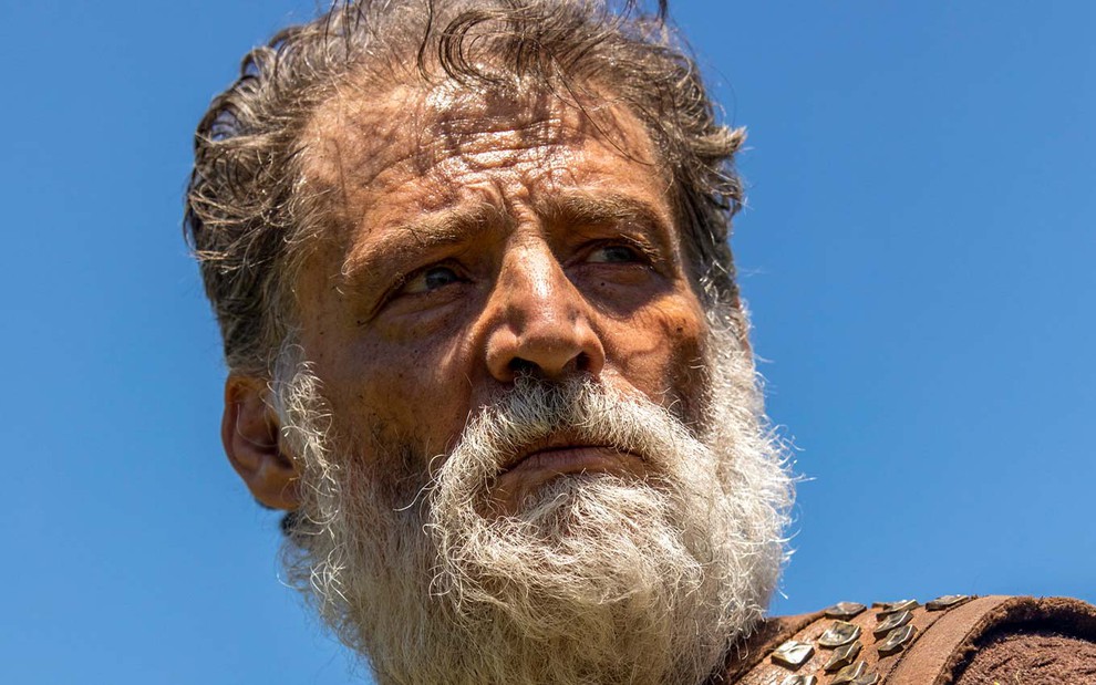 Giuseppe Oristanio em cena de Gênesis: ator usa barba branca, tem os cabelos desgrenhados e olha de maneira séria para o horizonte