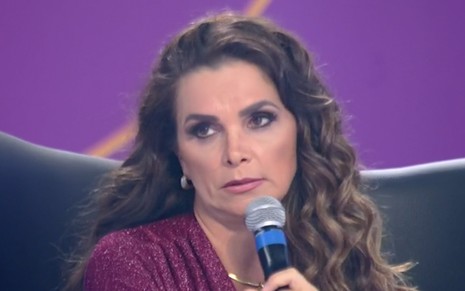 Luiza Ambiel sentada em uma poltrona preta com um microfone na mão na Hora do Faro