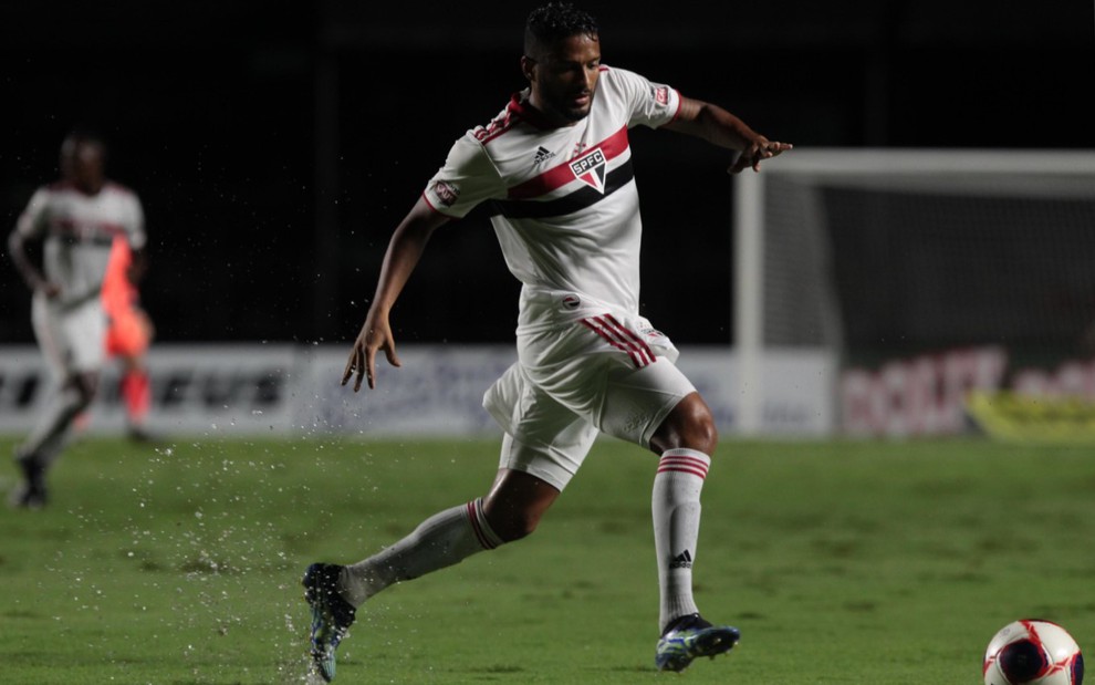 O jogador do São Paulo, Reinaldo, em lance no campo, vestido com o uniforme do time nas cores branco, vermelho e preto